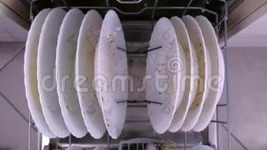 男人`手把一个白色的脏盘子放进洗碗机里，用厨房用具推篮子。
